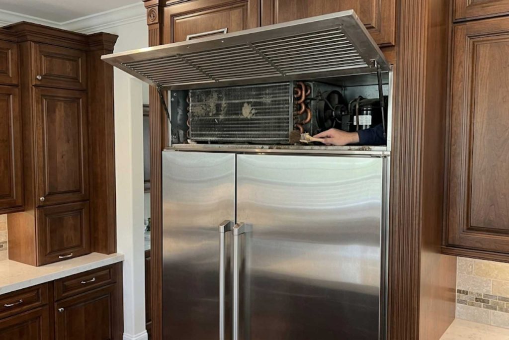 Upper grille lifted on a built-in GE Monogram refrigerator showing the condenser coils